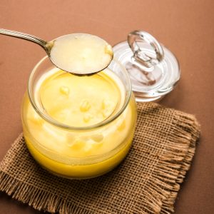 Ghee or clarified butter close up in wooden bowl and silver spoon, selective focus