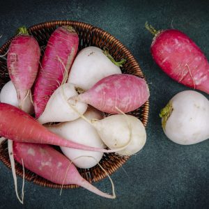 top view of white and pinkish red root vegetable beetroots on a bucket on a green background